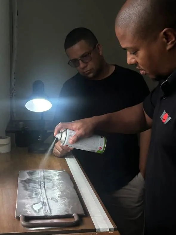 Aluno aplica o spray do ensaio por líquido penetrante numa chapa soldada, na bancada