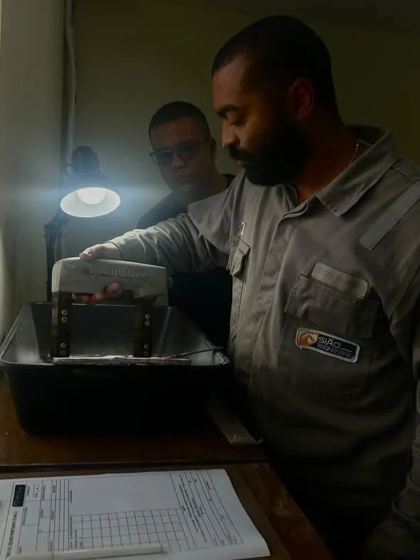Instrutor e aluno com uniforme da Sião junto ao equipamento do ensaio por partículas magnéticas